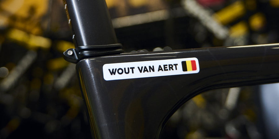Naamsticker van Wout van Aert op zijn fiets in de werkplaats, tussen de teamfietsen